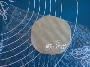 取一个冰皮面团，用手压扁或者用擀面杖擀扁。
如图我是用保鲜膜包着压的，这样可以解决很多人担心的粘手问题。