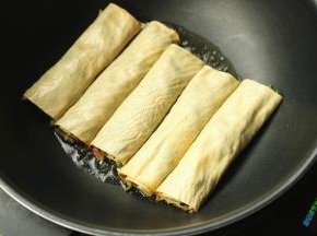 炒锅放油，下入豆皮肉卷开始煎制。