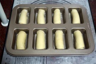 将卷好的坯子，放入金色方形8连杯不粘模具中，然后盖上保鲜膜，放入烤箱，启动发酵程序，进行二次发酵，耗时大概1个小时。