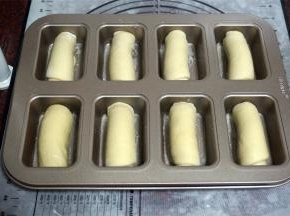 将卷好的坯子，放入金色方形8连杯不粘模具中，然后盖上保鲜膜，放入烤箱，启动发酵程序，进行二次发酵，耗时大概1个小时。