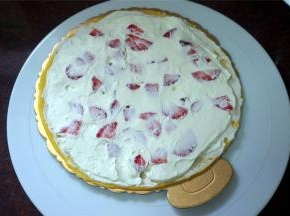 取一片班戟皮放在蛋糕底托上，然后挤上一圈圈的淡奶油，放入草莓粒，用刮刀抹平。