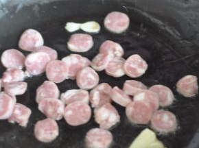 锅里倒入油，放入蒜片，放入香肠。