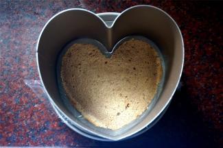 模具主体先用保鲜膜包裹底部，然后放在底托上。将剪裁好的心形蛋糕体放入模具中。