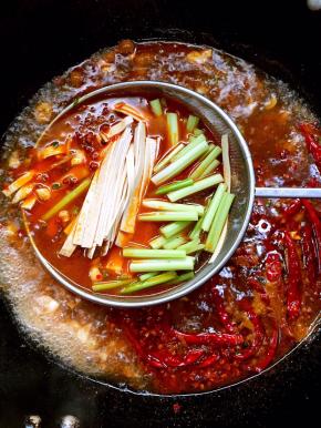 转大火，等红油汤水沸腾后，将洗净的西芹和千张放入漏勺里烫1分钟左右，迅速捞出。