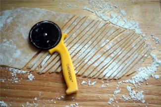 在面团上撒上玉米淀粉防粘，然后擀成0.2厘米厚的薄片。用披萨轮刀切成细坯条，在皮条上撒上玉米淀粉防粘。