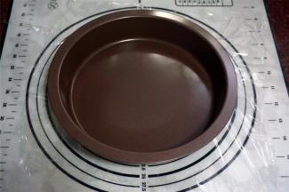 在面团上方铺上一片保鲜膜，然后用派盘中心按压面团至扁。