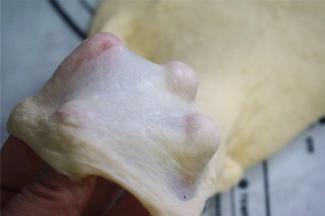 取出面团，检查筋性，能拉出薄膜即可。若仍然拉不出膜，可以撒上面团防粘，在硅胶垫上摔打增加筋性。