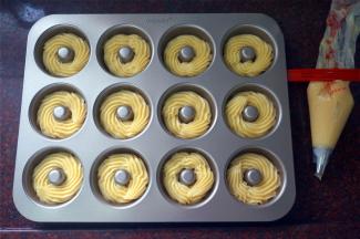 将面糊装入带菊花嘴的裱花袋，然后在12连甜甜圈模具中挤出面糊，如曲奇饼坯状。