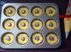 将面糊装入带菊花嘴的裱花袋，然后在12连甜甜圈模具中挤出面糊，如曲奇饼坯状。