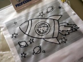 图案纸上放上透明的转印片，然后表面再放上一张糯米纸，用可食用色笔描绘图案。