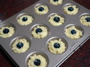 将蛋糕糊挤入模具中，挤1/2的量即可。放上一颗新鲜蓝莓，然后将酥粒均匀地撒到麦芬面糊顶部。