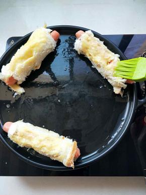 电陶炉启动煎烤，烤盘刷上油，放入香肠面包条，剩下的蛋液刷在面包上。