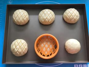 将包好的面团放入烤盘，用菠萝包印模压出花纹，盖保鲜膜放温暖湿润处进行第二次发酵。