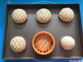 将包好的面团放入烤盘，用菠萝包印模压出花纹，盖保鲜膜放温暖湿润处进行第二次发酵。