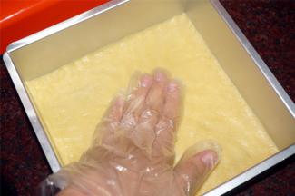 模具底部垫上一张与模具等大的吸油纸，然后将面团铺在模具底部，用手将面团压平整，压实。