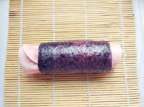 在寿司卷帘的辅助下，从一端卷起，边卷边用两手小指朝内推一下火腿片，直到卷成一个圆筒