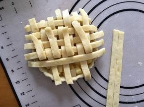 将剩余的派皮擀成薄片，用刀切成小长条，，在派盘表面编织出交叉的网格