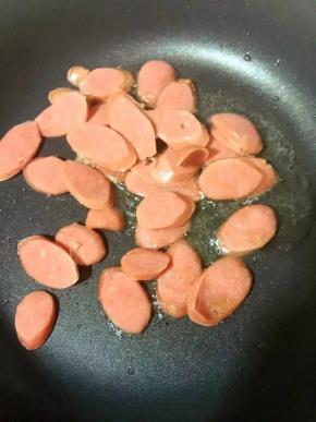 锅中倒入油烧热后转小火，倒入烤肠翻炒至边缘卷起