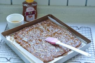 11、把翻过面的肉上，再刷一层蜂蜜水，撒上白芝麻，垫上油纸再用擀面杖擀平，送入烤箱继续烤制10分钟左右，变色即可。