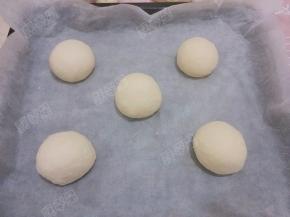 松驰好的面团再次用手轻压排气，再次滚圆，排放在铺了油纸的烤盘中