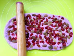 均匀的铺上葡萄干跟蔓越梅，果干可以根据个人喜好来放，也可以放干果，之后用擀面杖压一下果干，让果干黏紧在面团上，免得一会卷起的时候果干滚动