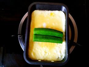 在蛋饼还没有彻底凝固的时候把两个秋葵并排摆放在蛋饼的中间位置。