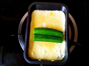 在蛋饼还没有彻底凝固的时候把两个秋葵并排摆放在蛋饼的中间位置。