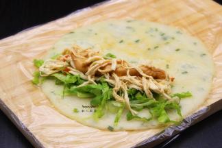 煎好的鸡蛋香葱饼，放入鸡丝肉、生菜、香葱、花生酱，卷起了，中间切段；