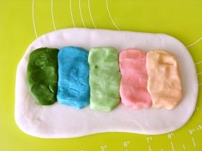 将水油皮面团擀成长方形，将5种颜色的油酥皮面团均匀揉成一样大小的长条，均匀的排列在水油皮上，颜色由浅至深排列