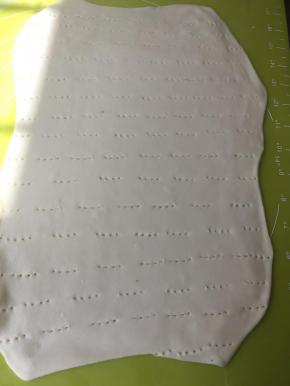 做了三次四折，以及松弛3次15分钟的面团，铺油纸，在油纸上擀成0.3厘米厚的长方形，用叉子扎些孔