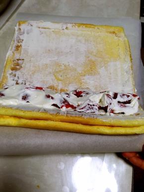 擀面杖将底下的油纸卷起，借用擀面杖的力量，将蛋糕卷顺势卷起来，收口处用擀面杖压一下底下的油纸，忘里面收一下，这样可以让蛋糕卷更紧实些