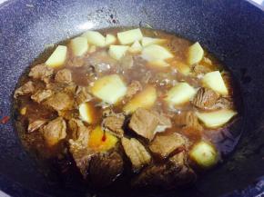 压好的牛肉连同汤汁倒回锅内，加入土豆块，继续炖煮