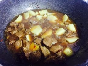 压好的牛肉连同汤汁倒回锅内，加入土豆块，继续炖煮