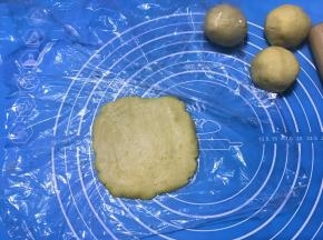 将冷藏松弛好的面团分成4份，取一份面团，上下铺保鲜膜覆盖，用擀面杖擀成薄片。