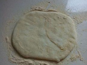 案板上放上一层黄豆粉，将其放上，上面再放上一层黄豆粉，用手压扁。