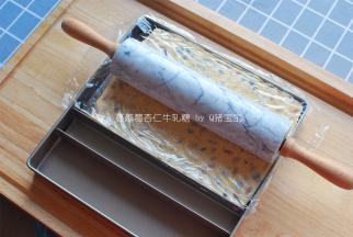 将牛轧糖转移到刷了油的11寸方形不粘烤盘中，借助加长款饼干模和大理石擀面杖以及保鲜膜进行整形。