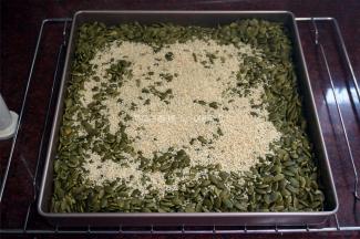 烤箱上下火转为100度，将烤熟的南瓜子同放入一个11寸不粘正方形烤盘中，然后加入白芝麻，放入烤箱中层保温。