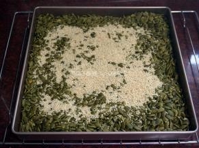 烤箱上下火转为100度，将烤熟的南瓜子同放入一个11寸不粘正方形烤盘中，然后加入白芝麻，放入烤箱中层保温。