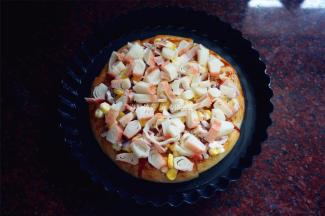 将调了味的玉米洋葱碎铺放在披萨皮上，再摆上蟹柳肉。