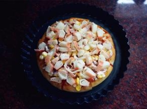 将调了味的玉米洋葱碎铺放在披萨皮上，再摆上蟹柳肉。