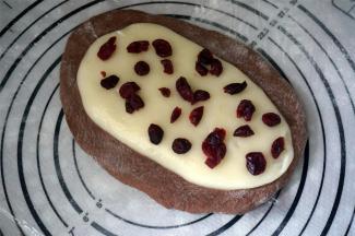 将可可面团擀扁成椭圆形，麻薯面团放在可可面团上，压开成稍细的椭圆形，并撒上少许蔓越莓干。