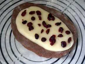 将可可面团擀扁成椭圆形，麻薯面团放在可可面团上，压开成稍细的椭圆形，并撒上少许蔓越莓干。