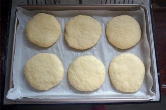 将松弛后的面团压扁成圆形，排在烤盘上，放在温暖处进行二次发酵。