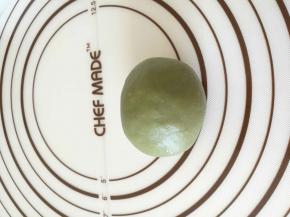 取出抹茶油皮，擀成圆形，包去上一步的油酥团，轻轻按压成椭圆形