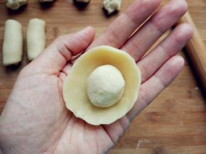 取一块水油皮，两手大拇指在内，其余手指在外，边捏边转动，形成一个中间凹的圆饼，把油酥团成球，放在中间。