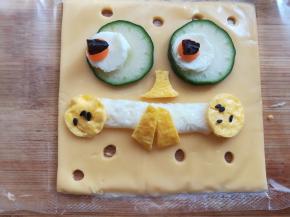 蛋白剪一小段做嘴巴，蛋黄部分剪出一个鼻子，2个嘴角和2个牙齿，拼在芝士上