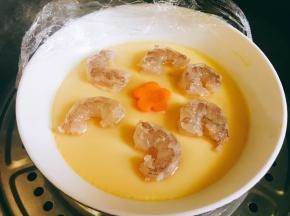 去掉保鲜膜之后放上虾和胡萝卜花瓣片，继续蒸两到三分钟