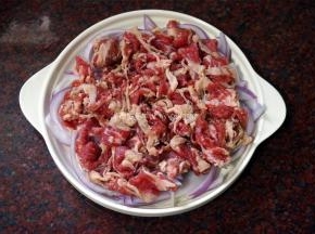 将腌制好的肥肉肉片铺到洋葱上。