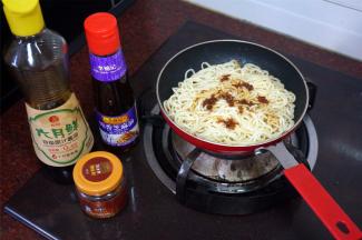 将煮好的面条倒入煎锅，小火加热，同时加入适量的酱油，XO酱，芝麻油，炒均匀。