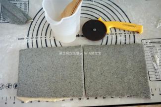 原味面片刷上一层水，将黑芝麻面片叠放在上面，然后刷上一层水，切去不规则的边沿，将面片分成两等分。